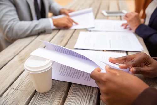 Business professionals reading agreement text in street cafe. Business people sitting at cafe table and studying documents. Contract expertise concept